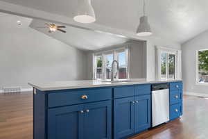 Kitchen with stainless steel dishwasher, vaulted ceiling, a sink, blue cabinets, and dark wood-style floors