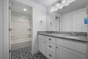 Full bathroom with double vanity, shower / bathtub combination, and baseboards