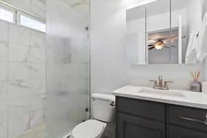 Full bath featuring toilet, vanity, a stall shower, ceiling fan, and baseboard heating