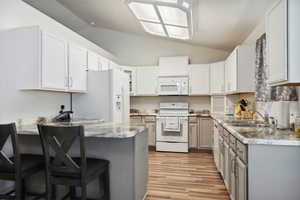 Kitchen featuring white appliances, a sink, lofted ceiling, a breakfast bar, and light wood-style flooring