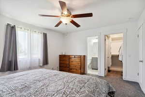 Carpeted bedroom with a spacious closet, a closet, a ceiling fan, ensuite bathroom, and baseboards
