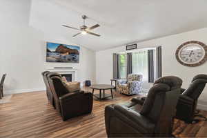 Living room featuring ceiling fan, lofted ceiling, wood finished floors, baseboards, and a glass covered fireplace