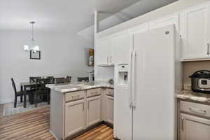 Kitchen with white refrigerator with ice dispenser, a peninsula, a chandelier, light wood finished floors, and pendant lighting