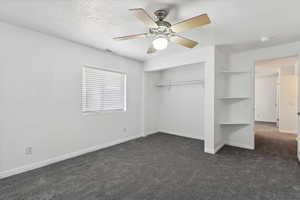 Unfurnished bedroom with dark colored carpet, a textured ceiling, a closet, baseboards, and ceiling fan
