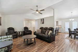 Living room featuring lofted ceiling, wood finished floors, ceiling fan, a chandelier, and baseboards