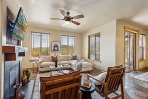 Living room featuring baseboards, a ceiling fan, a fireplace, and stone tile floors