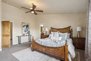 Carpeted bedroom with vaulted ceiling, ensuite bath, baseboards, and a ceiling fan