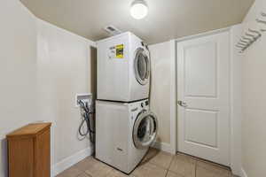 Laundry room with stacked washer / dryer, light tile patterned floors, and baseboards