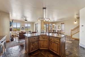 Kitchen with baseboards, stone tile floors, a ceiling fan, a center island, and brown cabinetry