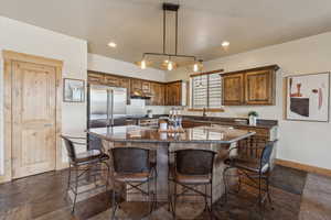 Kitchen with baseboards, under cabinet range hood, a sink, a center island, and a kitchen breakfast bar
