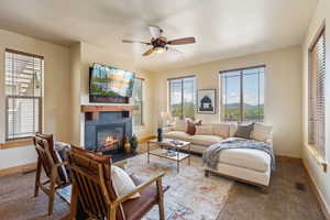 Carpeted living area featuring a fireplace, baseboards, and ceiling fan