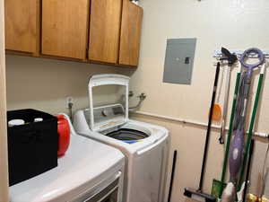 Laundry area with electric panel, washer and dryer, cabinet space, and a textured wall