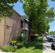 View of property exterior featuring a balcony, brick siding, and a lawn