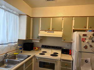 Kitchen with white appliances, under cabinet range hood, a sink, and light countertops