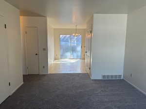 Carpeted family room looking into dinette room featuring a chandelier and baseboards