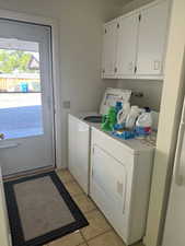 Laundry room featuring separate washer and dryer, light tile patterned flooring, and cabinet space