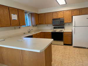 Kitchen with white appliances, brown cabinetry, light countertops, and a peninsula