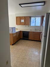 Kitchen with dishwasher, a sink, freestanding refrigerator, and brown cabinets