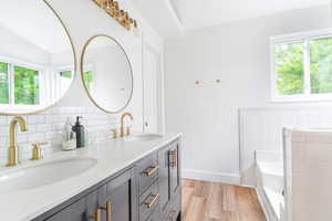 Full bath with wood finished floors, double vanity, decorative backsplash, a bath, and baseboards