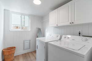 Laundry area featuring washing machine and clothes dryer, cabinet space, and light wood-type flooring