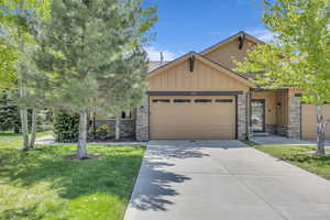Craftsman inspired home featuring stone siding, an attached garage, board and batten siding, a front lawn, and concrete driveway