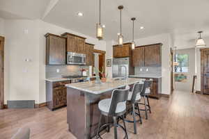 Kitchen featuring appliances with stainless steel finishes, tasteful backsplash, a breakfast bar area, a kitchen island with sink, and hanging light fixtures