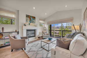 Living room with a glass covered fireplace, lofted ceiling, recessed lighting, and wood finished floors