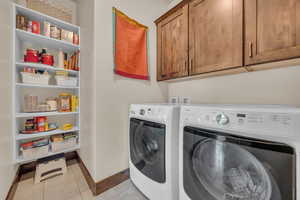 Laundry area with washing machine and clothes dryer, baseboards, cabinet space, and light tile patterned floors