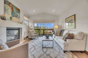 Living room with wood finished floors, vaulted ceiling, plenty of natural light, a glass covered fireplace, and baseboards