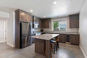 Kitchen featuring stainless steel appliances, beverage cooler, concrete flooring, a breakfast bar area, and recessed lighting