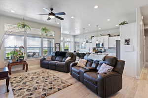 Living area with ceiling fan, recessed lighting, light wood-type flooring, baseboards, and a textured ceiling