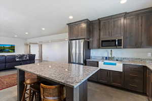 Kitchen featuring appliances with stainless steel finishes, a sink, concrete floors, dark brown cabinetry, and recessed lighting