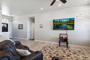 Living room with light wood-style floors, a chandelier, ceiling fan, baseboards, and recessed lighting