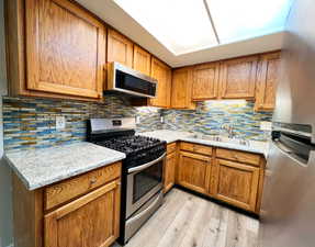 Kitchen with appliances with stainless steel finishes, a sink, light wood-type flooring, and brown cabinets