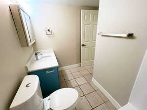 Half bath featuring toilet, vanity, tile patterned floors, and baseboards