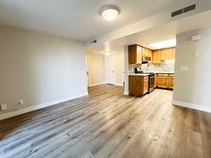 Kitchen with appliances with stainless steel finishes, baseboards, open floor plan, light wood-type flooring, and light countertops