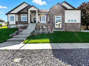 View of front facade featuring board and batten siding, stone siding, and a front lawn