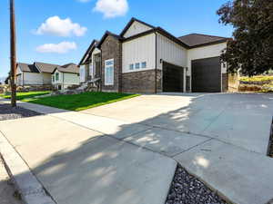 Modern farmhouse with an attached garage, board and batten siding, stone siding, driveway, and a front lawn