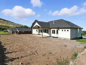 Back of house featuring a patio, a shingled roof, an attached garage, dirt driveway, and stucco siding