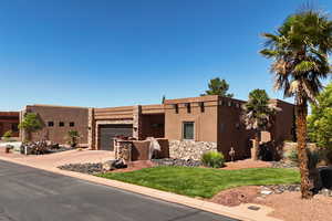 Southwest-style home with an attached garage, driveway, a front yard, stucco siding, and stone siding