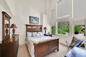 Bedroom with a high ceiling, multiple windows, baseboards, and light colored carpet