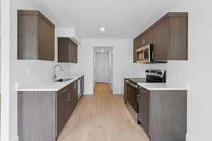 Kitchen featuring appliances with stainless steel finishes, dark brown cabinetry, light wood-style floors, light countertops, and recessed lighting