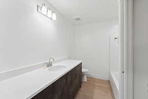 Bathroom with toilet, wood finished floors, vanity, a bathtub, and baseboards