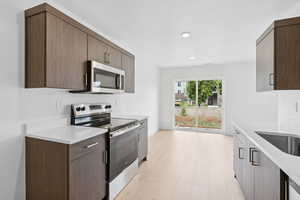 Kitchen with stainless steel appliances, light countertops, light wood-style floors, dark brown cabinets, and recessed lighting