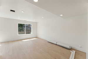 Empty room featuring light wood-style floors, baseboard heating, baseboards, and recessed lighting