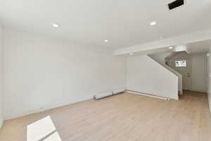 Below grade area with stairs, light wood finished floors, baseboards, and recessed lighting