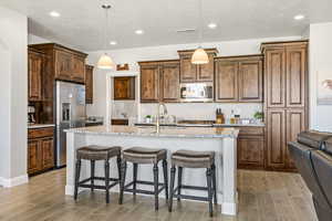 Kitchen with stainless steel appliances, light wood-style floors, a sink, a breakfast bar, and an island with sink