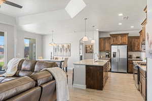 Kitchen featuring appliances with stainless steel finishes, open floor plan, a sink, ceiling fan, and light wood-type flooring