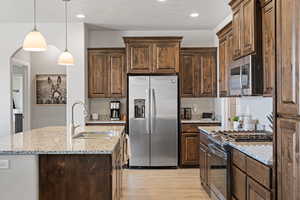 Kitchen with appliances with stainless steel finishes, a sink, light wood-type flooring, light stone countertops, and dark brown cabinets