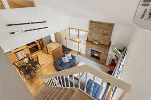 Living area with light wood-style floors, lofted ceiling, a stone fireplace, and stairway